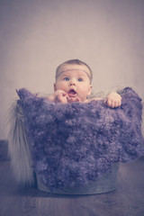 Fototapeta premium Portrait Baby sitzt im Eimer Hände Füße Fell lila vintage