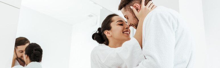 panoramic shot of happy girl smiling while hugging boyfriend in bathrobe