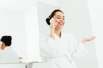 low angle view of happy young woman gesturing while talking on smartphone in bathroom