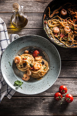 Pasta spaghetti on plate and pan with shrimp tomato sauce toatoes and herbs. Italian or mediterranean cuisine