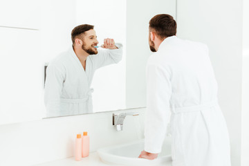 selective focus of handsome bearded man brushing teeth in bathroom