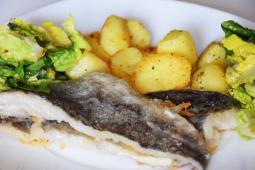 homemade dinner on a white plate baked potatoes fried fish cod, green lettuce with spices,