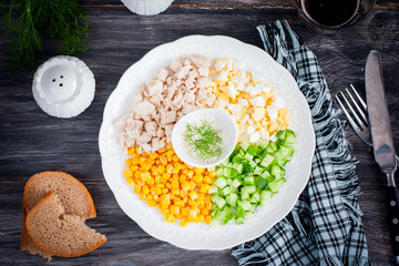 Corn salad, cucumber, egg, chicken on a white plate on a black table, top view, horizontal