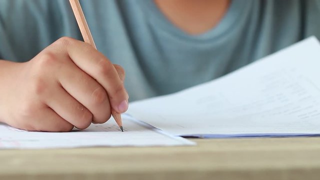 Education test exam concept, high school / university student holding pencil writing paper answer sheet on lecture chair for taking exams in examination room or classroom. Educational assessment ideas