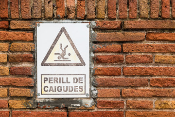 The sing with inscription 'Danger of falls' on a brick wall front view closeup