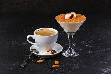 Traditional Italian dessert tiramisu, decorated with chocolate, sweets and toffee, in a martini and coffee glass of americano on a black background with walnuts and almonds