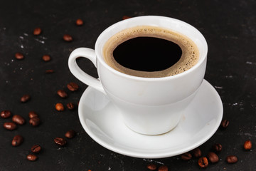 Black coffee, americano, espresso in a white mug with a saucer on a black background, coffee beans are scattered around