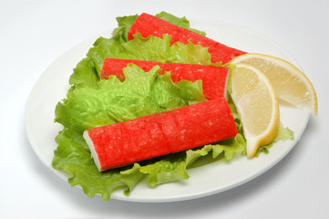 Crab sticks on a plate with salad, lemon slices on a white background