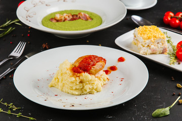 Multi-course business lunch: mashed potatoes with chicken breast, Russian traditional salad, green pea puree bacon  with black tea, on black background