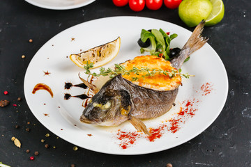 stuffed fish with carrots, parsley, horseradish and salad on a white plate, with tomatoes, lime, fork and knife, with a glass of white wine on a black background