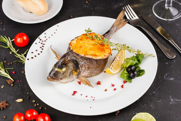 stuffed fish with carrots, parsley, horseradish and salad on a white plate, with tomatoes, lime, fork and knife, with a glass of white wine on a black background