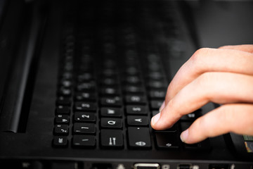 Fototapeta na wymiar Male hand typing on black computer desktop keyboard with shallow depth of field