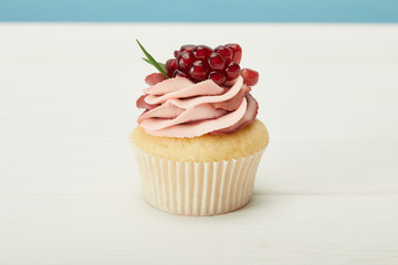 tasty cupcake with garnet and cream on white surface isolated on blue