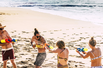 Youthful and people having fun outdoor at the beach for tropical summer holiday vacation at the sea - playing with water guns all together - couples and joyful concept
