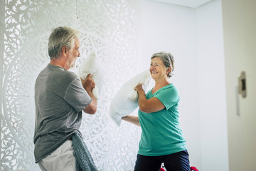 Happy cheerful old senior caucasian couple play at home with pillows in the bedroom - playful and...