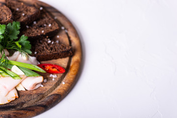 Lard, black bread and greens on a wooden board on a white background. Copy space.