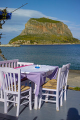 Traditional greek tavern with wooden tables on beach near water waiting for tourists in Monemvasia, Peloponnese, Greece