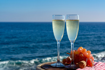 Champagne, prosecco or cava served with pink grape in two glasses on outside terrace with sea view