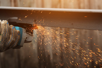 Industrial worker cutting metal with many sharp sparks working on angle grinder with circular blade