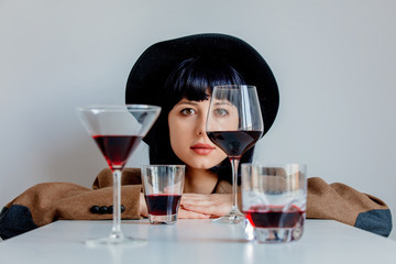 Brunet woman in hat near glasses of wine on white background