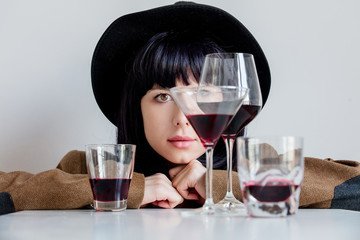 Brunet woman in hat near glasses of wine on white background