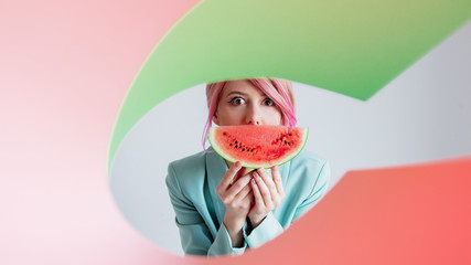 portrait of a young girl with pink hair in formal clothes of the 80s with a slice of watermelon with green nad pink paper