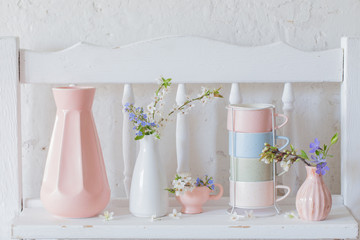 cups and vases with spring flowers on vintage wooden white shelf