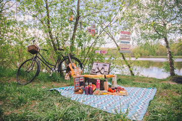 Fototapeta na wymiar Design summer picnic in nature. On the plaid is a basket of food. On the background of a bicycle and decorative ornaments