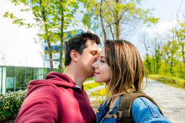 A young couple of Europeans kisses on the street. University building in the background. Spring time