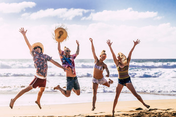Summer holiday vacation travel concept with young group of people friends jumping for happiness and joy at the beach with blue sea and sky in background enjoying nature and  outdoor free 