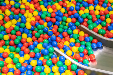 Fototapeta na wymiar Metal baby slide going down to the pool with many colored balls in the kids playing room.