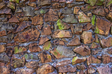 Old texture of stacked stone wall have bright green moss along the rock.