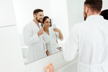 Obraz premium selective focus of cheerful woman taking photo with happy man holding toothbrush