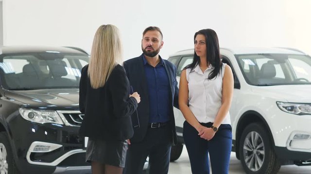 Cavcasian saleswoman with clipboard talking with couple choosing car at dealership