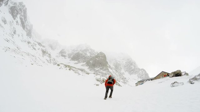 4K traveller with backpack wearing red coat scaling Ben Nevis reaching CIC Hut in early spring