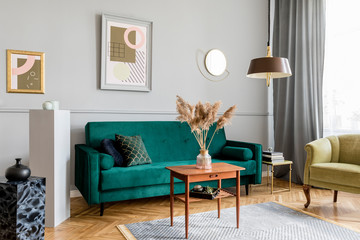Stylish and tasty living room of apartment interior with elegant green velvet armchair and sofa, brwon table, design lamp and chic accessories. Abstract paintings on the gray wall. Luxury home decor.