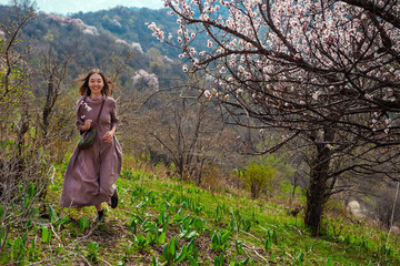 An Asian girl outdoors runs among flowering trees. Spring time