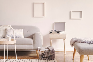 Stylish and cozy scandinavian white interior with design sofa, bench, coffee table, pillows, blanket, gramophone and mock up photo frames. White background walls and modern space. 