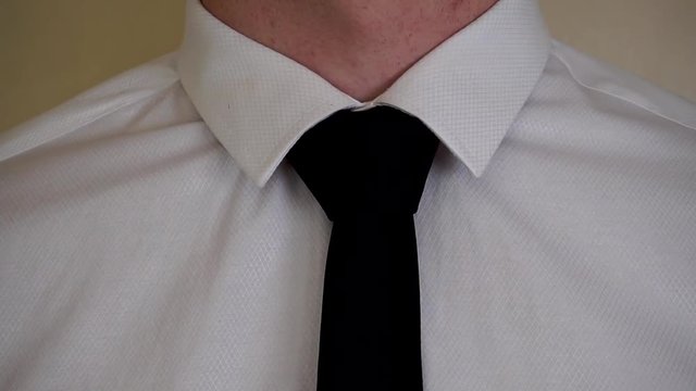 Young caucasian man fixing black tie wearing white shirt close up