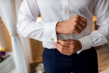 A groom putting on cufflinks as he gets dressed in formal wear. Man getting ready for work.