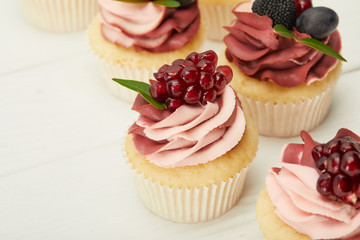 selective focus of cupcakes with cream and berries on white surface