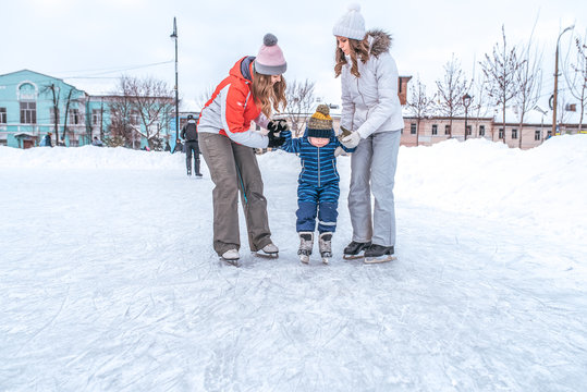 A young mother with a girlfriend is taught to skate little boy. In the winter in the city on the ice rink. In winter sportswear.