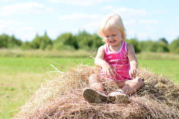 Naklejka na ściany i meble Happy baby girl laughing on summer haystack