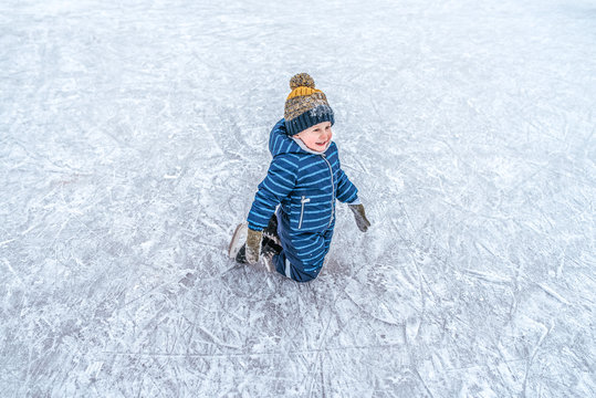 A little boy is on his knees, in winter, on a skating rink in winter overalls and a hat, he is smiling happily, first steps are on the ski carts. Joy and fun in the New Year holidays.