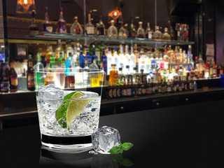 A glass of gin tonic or vodka lime with ice on bar counter and blurry bottles background - obrazy, fototapety, plakaty