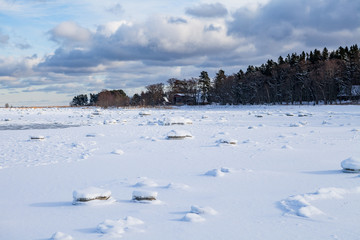 Frozen coast of Baltic sea covered by snow. Boulders, horizon and forest