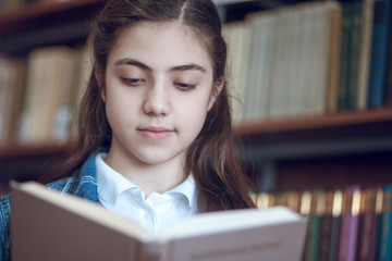 beautiful schoolgirl in the library reading a book