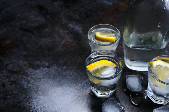 Vodka. Shots, glasses with vodka and lemon with ice .Dark stone background.