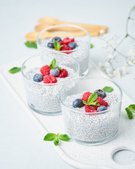 Chia pudding with fresh berries raspberries, blueberries. Three glass, light background, side view, flowers, vertical.