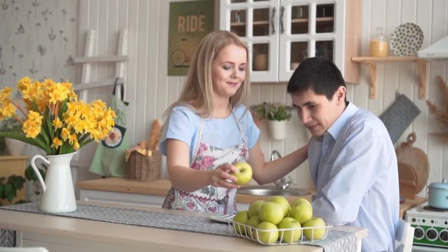 Young and happy couple in the kitchen. Happy couple in the kitchen. A young woman offers her boyfriend a green apple, together they hold an apple in their hands.